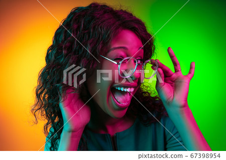 African-american young woman's portrait isolated on gradient yellow-green background in neon light 67398954