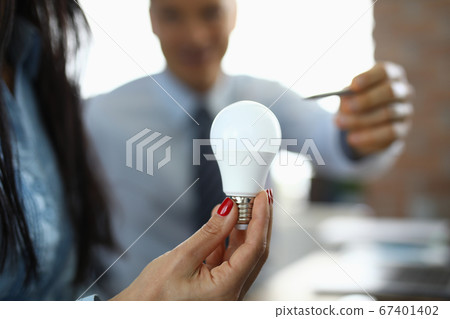 Woman in office holds light bulb in her hand. 67401402