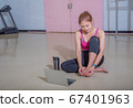 An athletic woman in a sports suit was sitting on the floor with a bottle of water and used a laptop at the gym. Sports and recreation concepts. 67401963