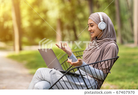 Pretty muslim girl having video conference while resting at park Pretty muslim girl having video conference while resting at park 67407970