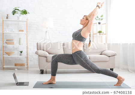 Fitness at home online. Woman in sportswear on sports mat with laptop in living room Fitness at home online. Woman in sportswear on sports mat with laptop in living room 67408138