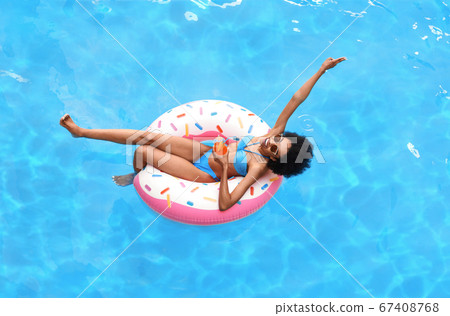 Attractive black woman with glass of summer cocktail on inflatable ring at pool, above view Attractive black woman with glass of summer cocktail on inflatable ring at pool, above view 67408768