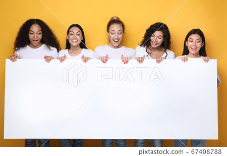 Excited Girls Holding Empty Poster For Text, Yellow Background, Mockup 67408788