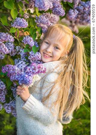 Little girl smelling lilac flowers in sunny day. Little girl smelling lilac flowers in sunny day. 67409559