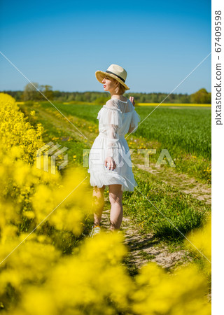 Young woman stands in a rape field 67409598