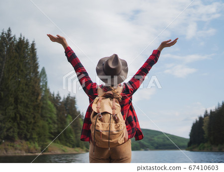 Rear view of young woman by lake on a walk outdoors in summer nature, relaxing. Rear view of young woman by lake on a walk outdoors in summer nature, relaxing. 67410603