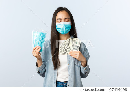 covid-19 pandemic, coronavirus expences and finance concept. Satisfied greedy asian girl in medical mask hugging money and showing masks, earn cash during coronavirus lockdown covid-19 pandemic, coronavirus expences and finance concept. Satisfied greedy asian girl in medical mask hugging money and showing masks, earn cash during coronavirus lockdown 67414498