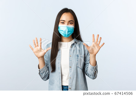 Social distancing lifestyle, covid-19 pandemic and people emotions concept. Smiling cheerful asian woman in medical mask showing ten fingers, empty hands, white background Social distancing lifestyle, covid-19 pandemic and people emotions concept. Smiling cheerful asian woman in medical mask showing ten fingers, empty hands, white background 67414506