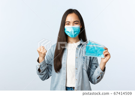 Social distancing lifestyle, covid-19 pandemic everyday life and leisure concept. Encouraged asian girl showing medical masks and fist as determined protect from coronavirus, sit home self-isolation Social distancing lifestyle, covid-19 pandemic everyday life and leisure concept. Encouraged asian girl showing medical masks and fist as determined protect from coronavirus, sit home self-isolation 67414509