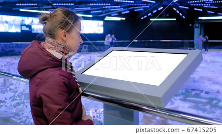 Woman looking at blank white display kiosk at exhibition - white screen concept Woman looking at blank white display kiosk at exhibition - white screen concept 67415205