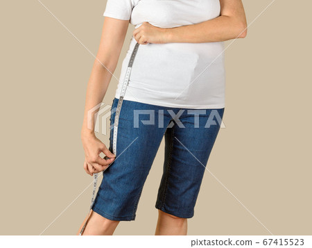 Caucasian mature adult woman measuring a blue denim capris before shortening. Caucasian mature adult woman measuring a blue denim capris before shortening. 67415523