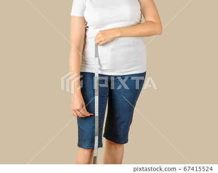 Caucasian mature adult woman drawing a cut line on a blue denim capris before shortening Caucasian mature adult woman drawing a cut line on a blue denim capris before shortening 67415524