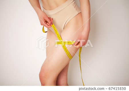 Woman with a sporty figure measures the size of her leg Woman with a sporty figure measures the size of her leg 67415830