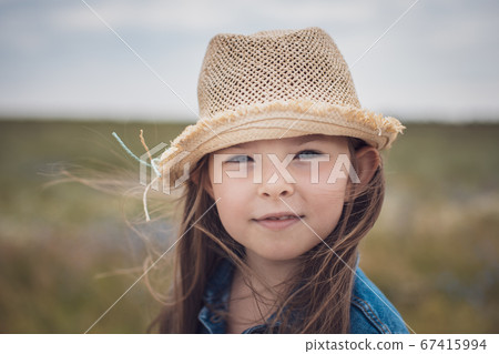 Portrait of a beautiful little girl in a straw hat and denim jacket against the backdrop of a rural road. Portrait of a beautiful little girl in a straw hat and denim jacket against the backdrop of a rural road. 67415994