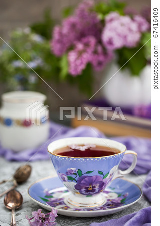 Purple cup of tea and lilac on gray background 67416409