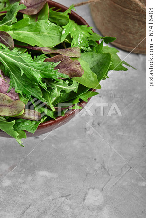Mix salad leaves in a brown bowl over dark slate, stone or concrete background. Top view with copy space. Mix salad leaves in a brown bowl over dark slate, stone or concrete background. Top view with copy space. 67416483