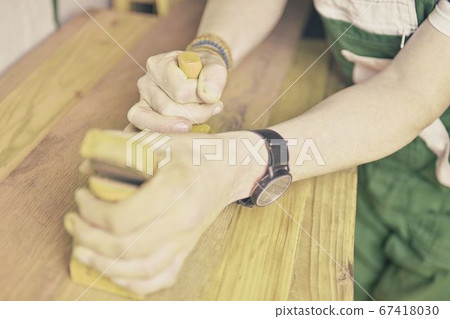 Carpenter working with plane on table in his workshop. Carpenter working with plane in a carpentry shop. Young carpenter wearing bracelets Carpenter working with plane on table in his workshop. Carpenter working with plane in a carpentry shop. Young carpenter wearing bracelets 67418030