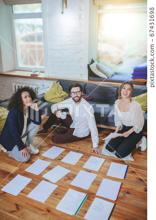 Three smiling young friends near papers on the floor. 67431698