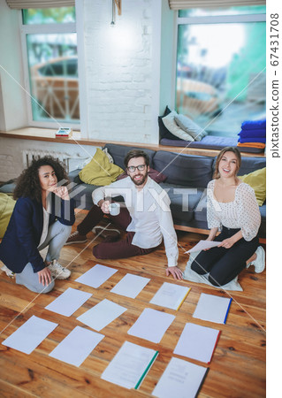 Guy with coffee, two girls on floor near spread out documents 67431708