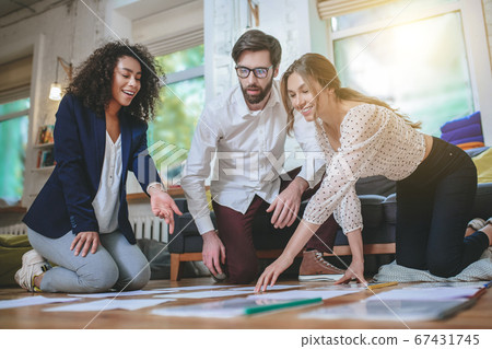 Cheerful girls and thoughtful guy laying documents on the floor. Cheerful girls and thoughtful guy laying documents on the floor. 67431745