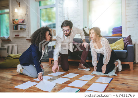 Guy and two girlfriends in room on floor working on project 67431769