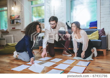 Serious guy with glasses and two girls laying papers on floor 67431786