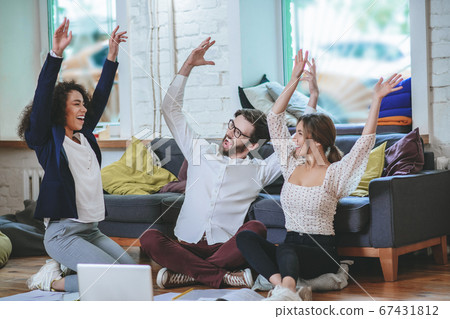 Guy and two girls sitting on floor with their hands up Guy and two girls sitting on floor with their hands up 67431812