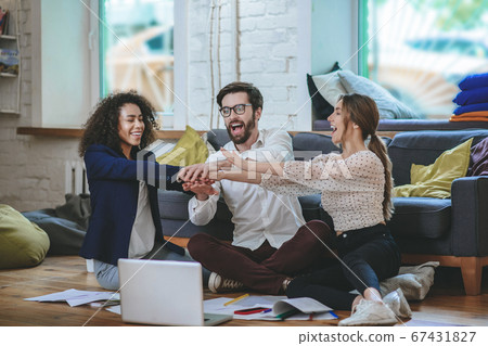 Three young friends colleagues sitting on floor in room Three young friends colleagues sitting on floor in room 67431827