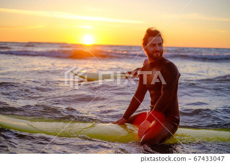 Surfer sitting on surfboard in sea Surfer sitting on surfboard in sea 67433047