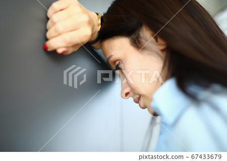 Sad woman is standing against wall with her elbow on her arm Sad woman is standing against wall with her elbow on her arm 67433679
