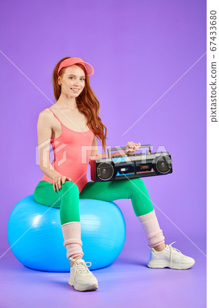 athletic female dancer sits on fit ball with portable cassette player on knees athletic female dancer sits on fit ball with portable cassette player on knees 67433680