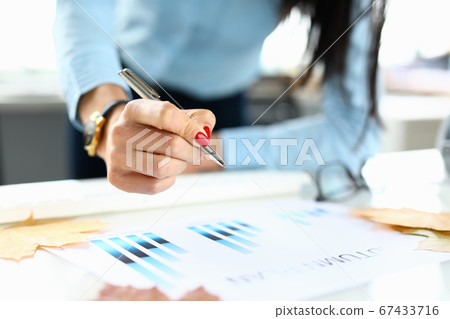 Woman in office holds a pen in her hand over chart Woman in office holds a pen in her hand over chart 67433716