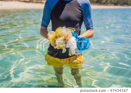Man collects packages from the beautiful turquoise sea. Paradise beach pollution. Problem of spilled rubbish trash garbage on the beach sand caused by man-made pollution and environmental, campaign to Man collects packages from the beautiful turquoise sea. Paradise beach pollution. Problem of spilled rubbish trash garbage on the beach sand caused by man-made pollution and environmental, campaign to 67434587