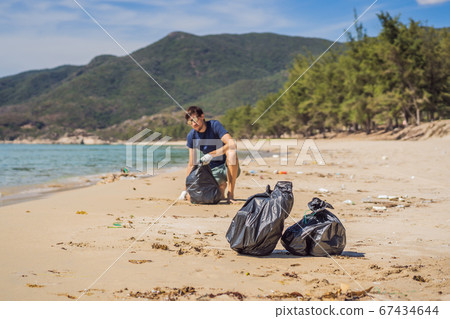 Man in gloves pick up plastic bags that pollute sea. Problem of spilled rubbish trash garbage on the beach sand caused by man-made pollution and environmental, campaign to clean volunteer in concept 67434644