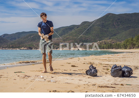 Man in gloves pick up plastic bags that pollute sea. Problem of spilled rubbish trash garbage on the beach sand caused by man-made pollution and environmental, campaign to clean volunteer in concept Man in gloves pick up plastic bags that pollute sea. Problem of spilled rubbish trash garbage on the beach sand caused by man-made pollution and environmental, campaign to clean volunteer in concept 67434650