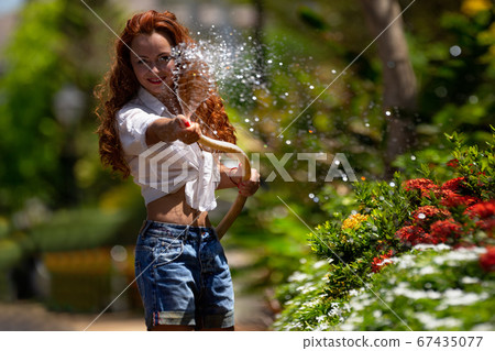 Woman is watering flowers in a garden Woman is watering flowers in a garden 67435077