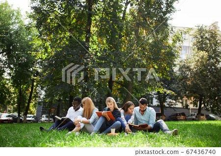 Mixed-race group of students sitting together on green lawn of university campus Mixed-race group of students sitting together on green lawn of university campus 67436740