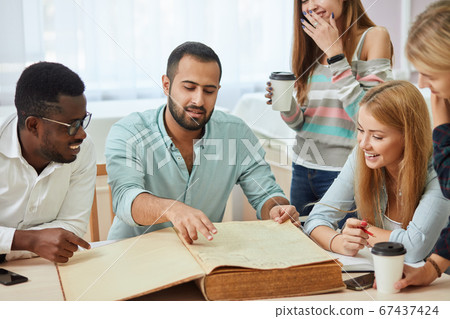 Diverse multiracial students spending leisure time in library with big old book 67437424