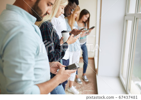 Series photo of group multiethnic hipster teenagers friends looking in smart phones while sitting on the bench outdoor in city center.People, leisure, friendship, technology and communication concept Series photo of group multiethnic hipster teenagers friends looking in smart phones while sitting on the bench outdoor in city center.People, leisure, friendship, technology and communication concept 67437481