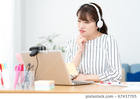 Telework A young woman with a slightly embarrassed face who is having a web conference with white headphones at home 67437705