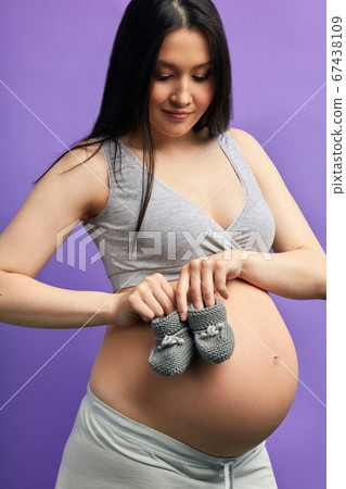 Baby booties for unborn child on the belly of pregnant woman posing indoors Baby booties for unborn child on the belly of pregnant woman posing indoors 67438109