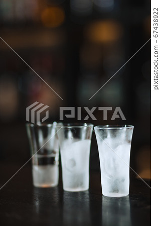 Three clean frosten short glasses with vodka stand on ice crumbs on bar stand. Three clean frosten short glasses with vodka stand on ice crumbs on bar stand. 67438922