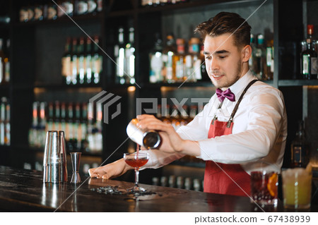 Barman pouring fresh cocktail from shaker into the glass on the bar counter 67438939