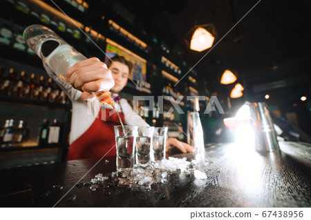 Hands of bartender pouring some drink into shot glasses on a wooden counter Hands of bartender pouring some drink into shot glasses on a wooden counter 67438956