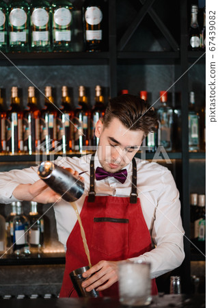 Barman pouring fresh cocktail from shaker into the glass on the bar counter Barman pouring fresh cocktail from shaker into the glass on the bar counter 67439082