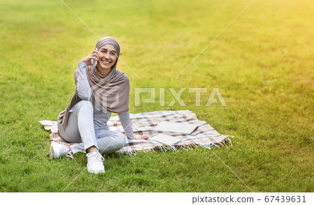 Positive muslim woman spending weekend at park Positive muslim woman spending weekend at park 67439631