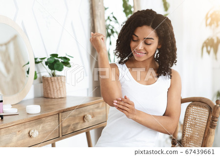 Dry Elbows Treatment. Smiling Black Woman Applying Moisturising Cream At Home Dry Elbows Treatment. Smiling Black Woman Applying Moisturising Cream At Home 67439661
