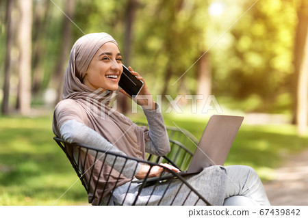 Young muslim woman talking on phone and using laptop 67439842