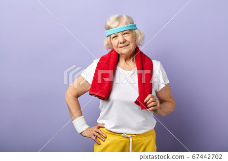 Elderly sportswoman with headband and red towel on neck, looking at camera Elderly sportswoman with headband and red towel on neck, looking at camera 67442702