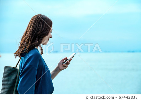 在海上操作智能手機的年輕女子 在海上操作智能手機的年輕女子 67442835
